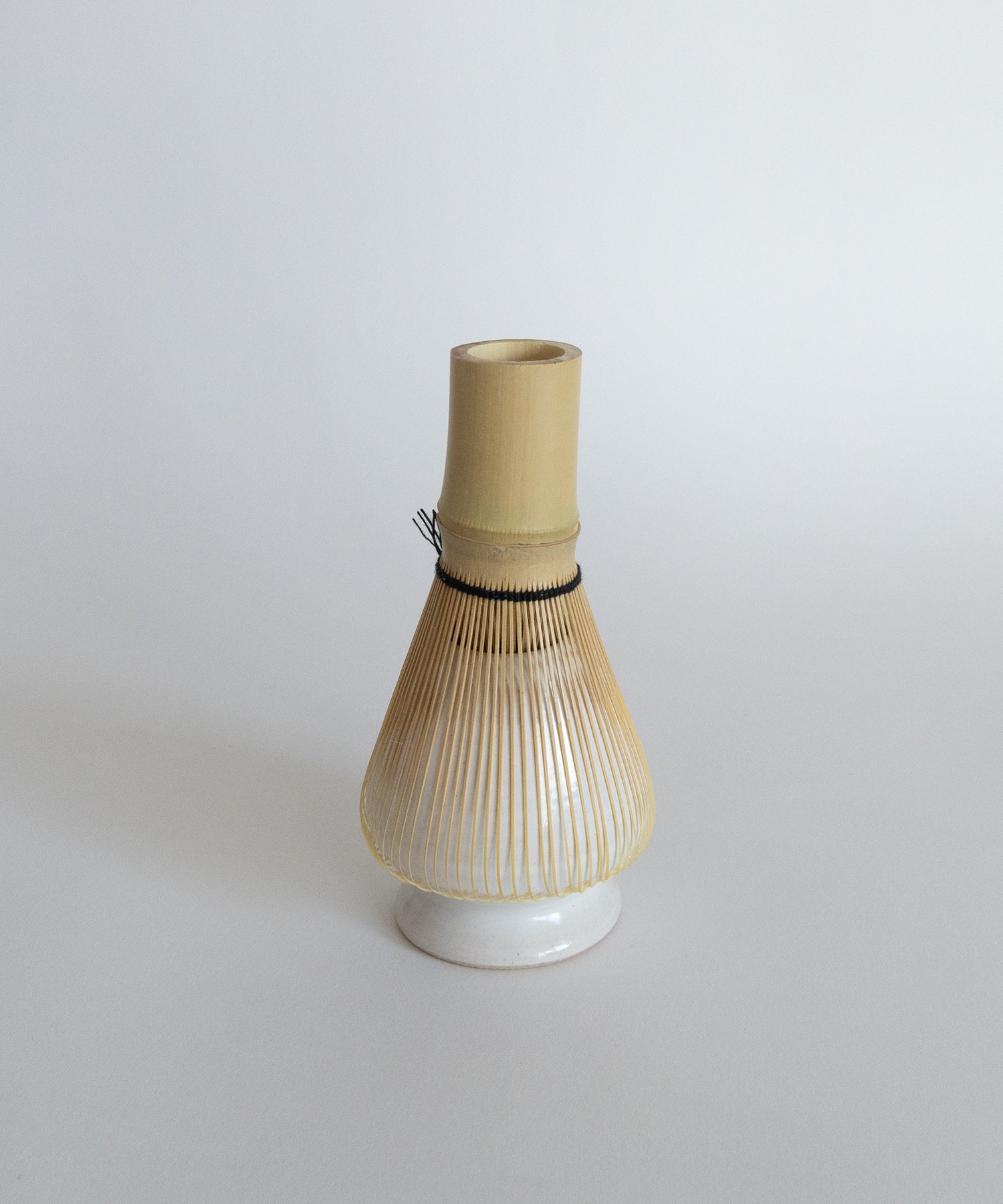 Bamboo whisk resting on a white whisk holder, promoting proper drying and shape retention.