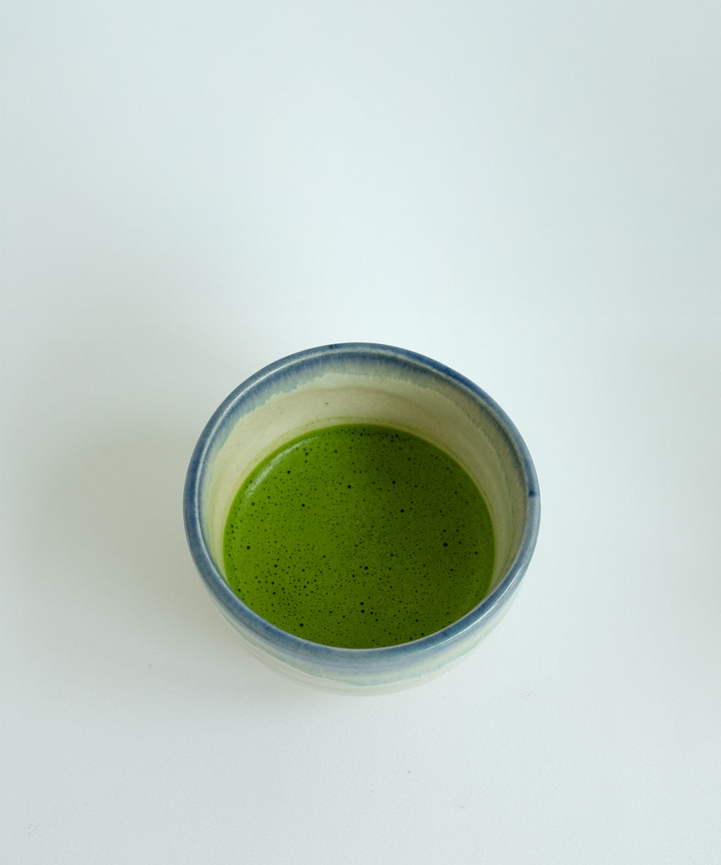 Top view of Japanese Mino pottery matcha bowl filled with ceremonial grade matcha, white blue rim glaze handmade ceramic bowl