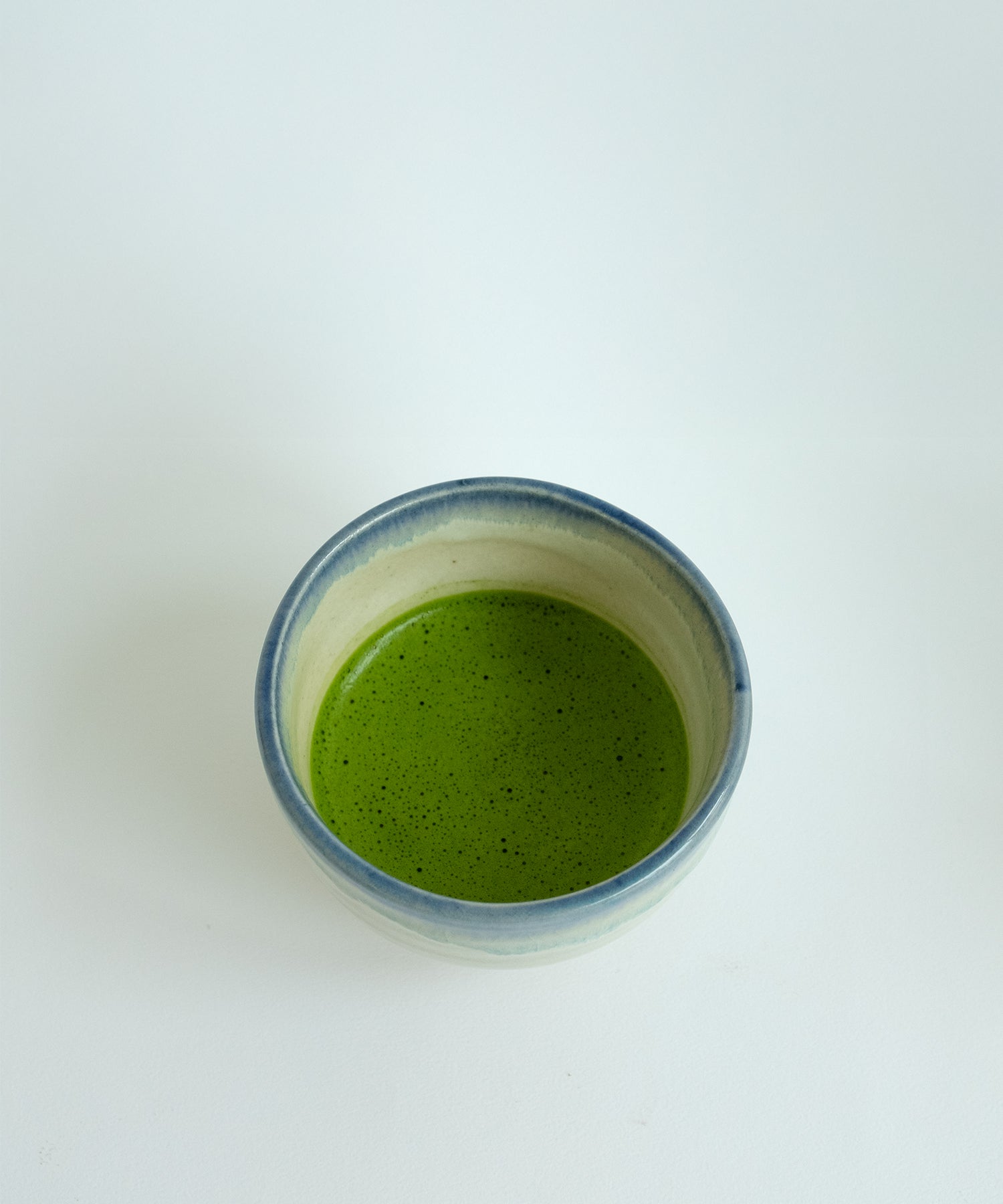 Top view of Japanese Mino pottery matcha bowl filled with ceremonial grade matcha, white blue rim glaze handmade ceramic bowl